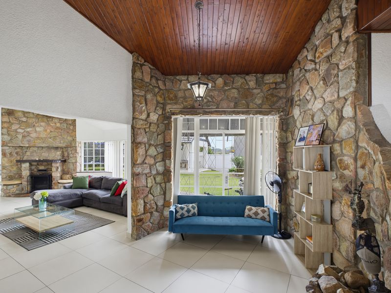 Spacious open-plan living area featuring distinctive natural stone feature walls, timber-clad vaulted ceilings, and large windows overlooking the garden.