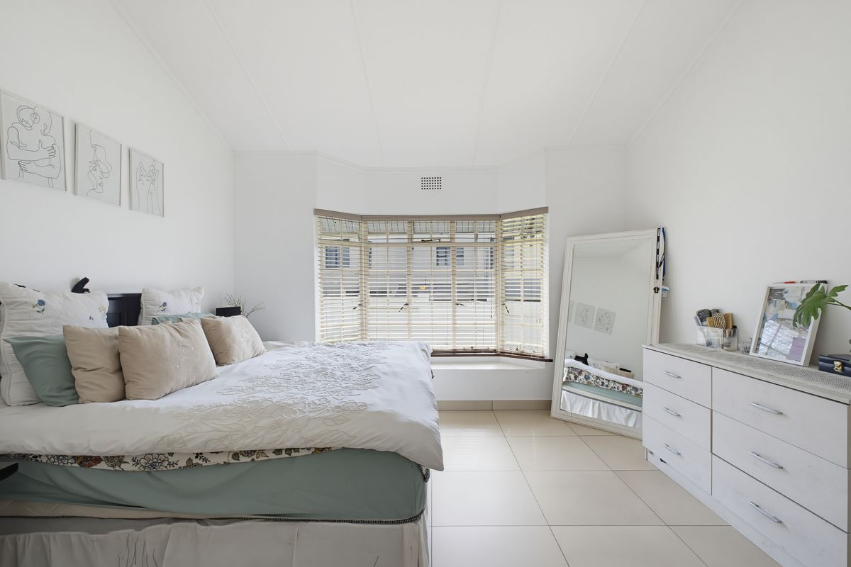 A bright bedroom featuring a large bay window with fitted blinds and neutral tiled flooring.