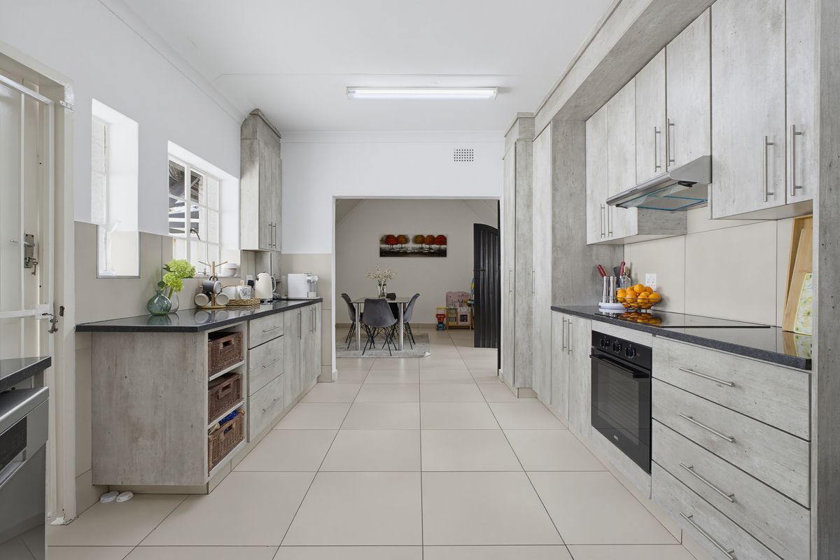 Modern galley-style kitchen featuring light wood-grain cabinetry, dark stone countertops, built-in oven, glass hob, and stainless steel extractor fan with tiled flooring.