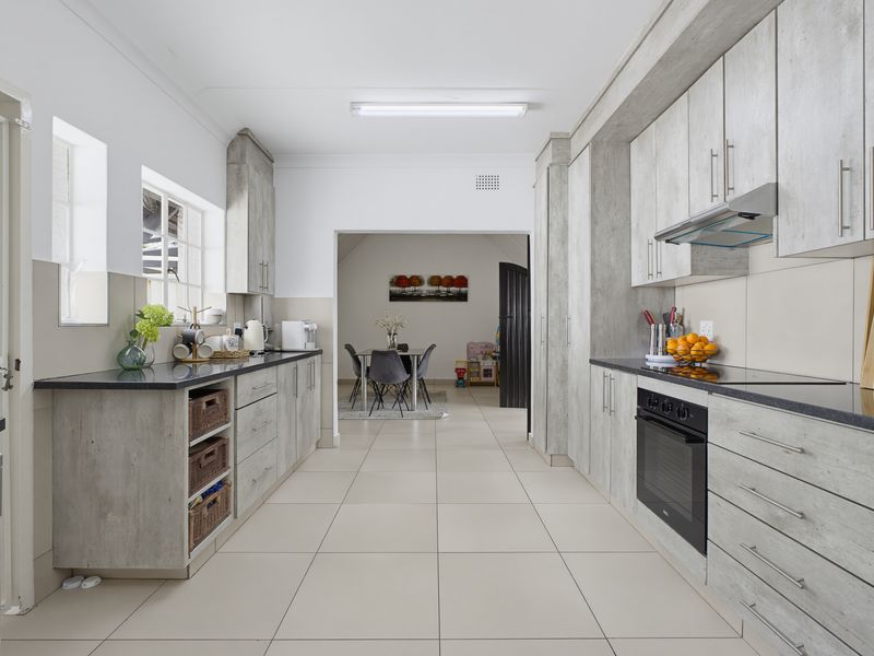 Modern galley-style kitchen featuring light wood-grain cabinetry, dark stone countertops, built-in oven, glass hob, and stainless steel extractor fan with tiled flooring.