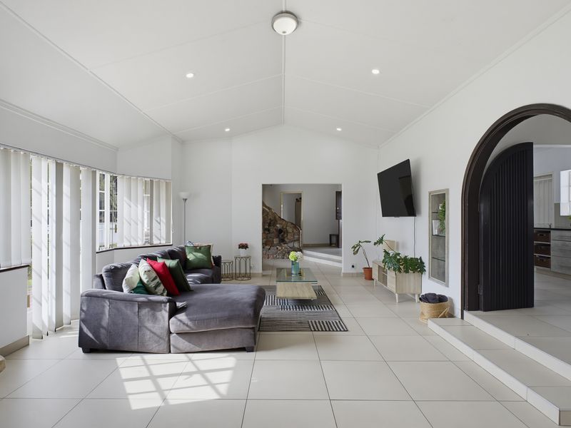 Spacious open-plan living area featuring vaulted ceilings, tiled flooring, and a distinctive arched doorway leading to the kitchen.