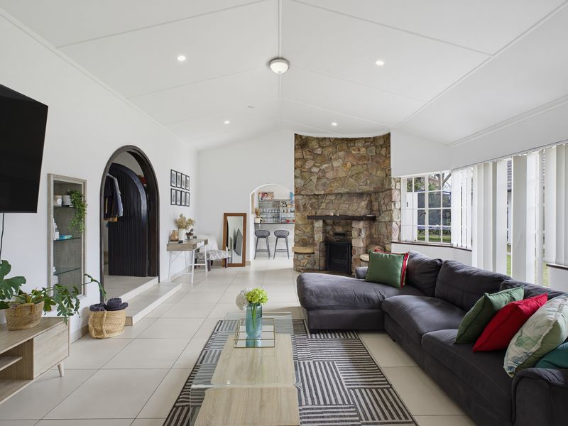 Spacious open-plan living area featuring a vaulted ceiling, tiled flooring, and a prominent stone-clad fireplace as a central architectural focal point.