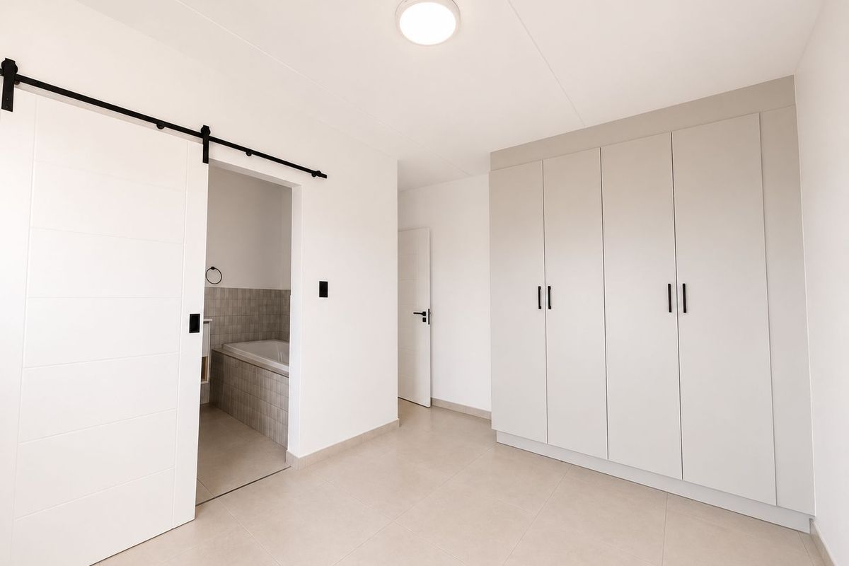 A bright bedroom featuring built-in floor-to-ceiling wardrobes, tiled flooring, and a sliding barn door providing access to an en-suite bathroom.