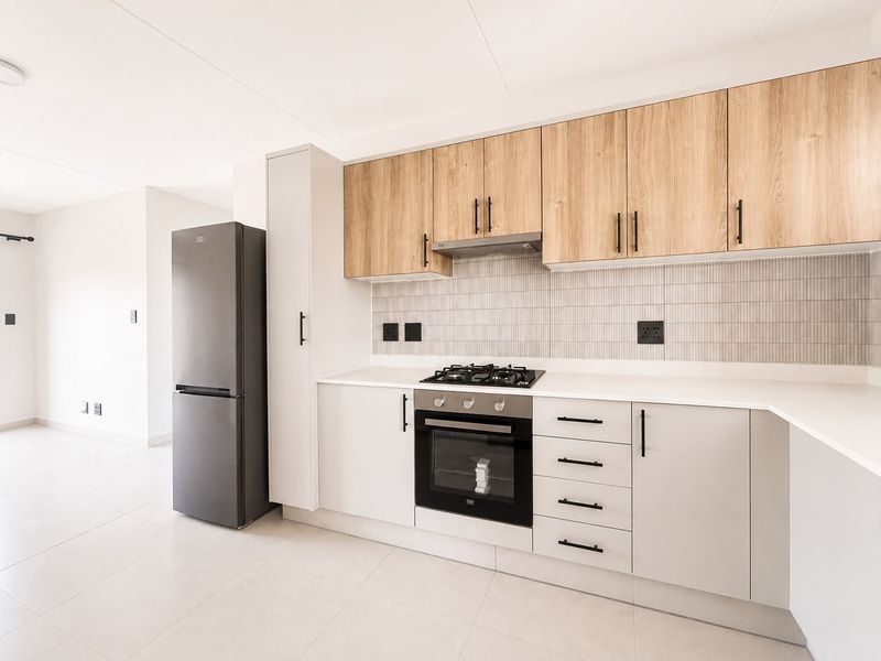 Modern kitchen featuring light wood-tone upper cabinets, white lower cabinetry, stone countertops, gas hob, and integrated oven with a clean tiled backsplash.
