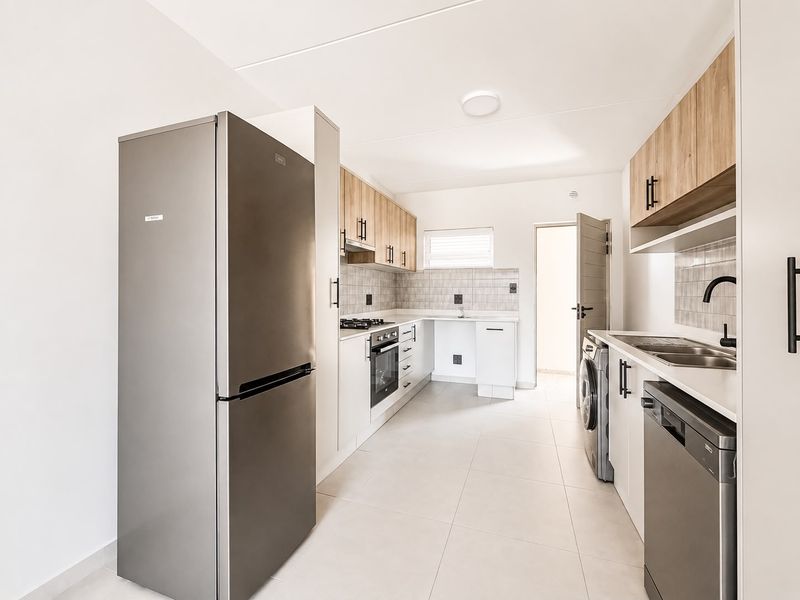Modern kitchen featuring light wood-tone cabinetry, tiled backsplash, built-in gas hob, oven, and integrated laundry and dishwasher plumbing connections.