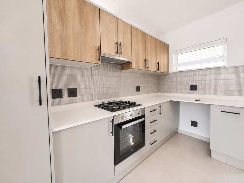 Modern kitchen featuring light wood-tone upper cabinets, neutral lower cabinetry, stone countertops, integrated gas hob, oven, and stylish tiled backsplash.
