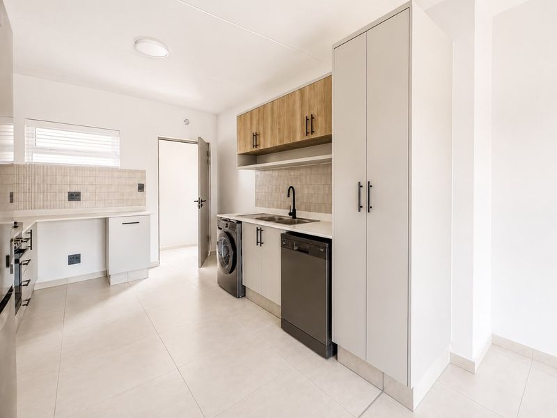 Modern kitchen featuring sleek cabinetry, light-toned countertops, a tiled backsplash, and integrated storage, offering a clean and functional workspace.