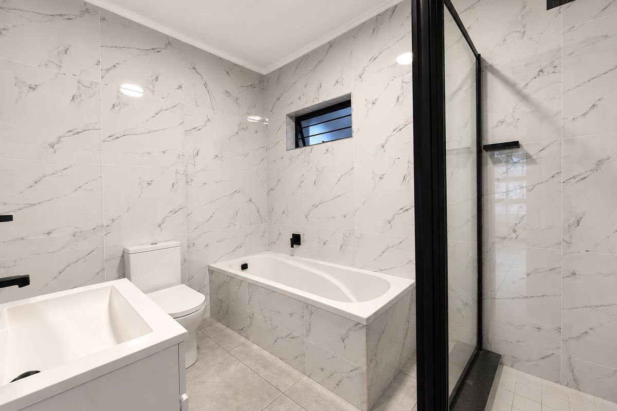Modern bathroom featuring marble-look wall tiles, a built-in bathtub, a separate glass-enclosed shower, and a contemporary vanity unit with matte black fixtures.