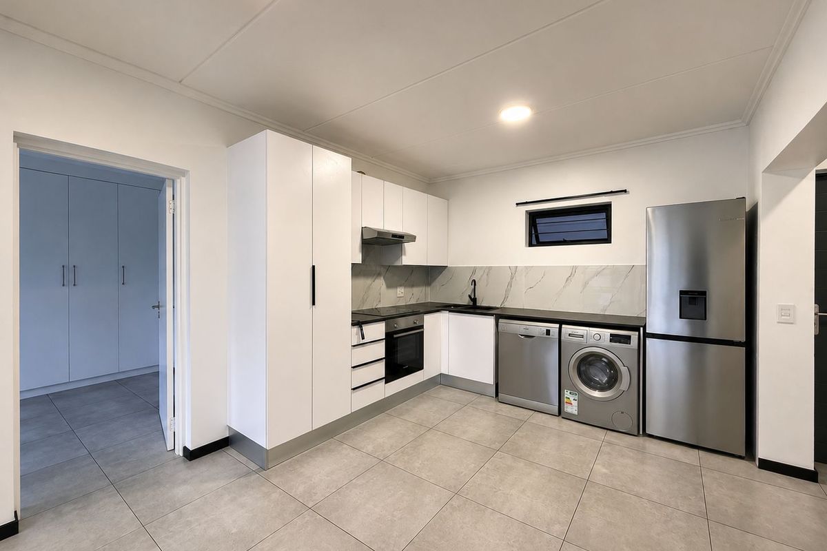 Modern kitchen featuring white cabinetry, marble-look splashback, integrated oven and hob, and tiled flooring, with adjacent laundry area and built-in storage.