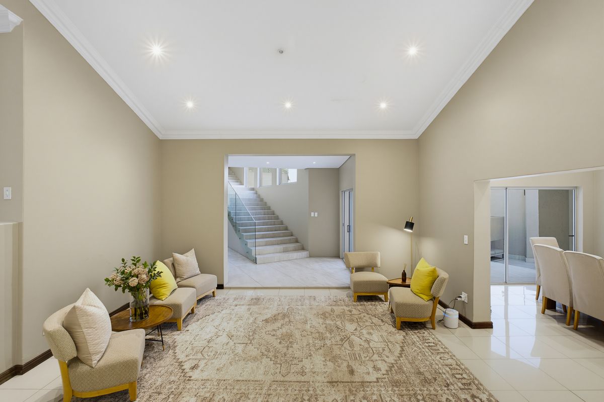 A spacious living area featuring neutral walls, recessed downlighting, crown molding, and polished tile flooring, with a view toward an internal staircase.
