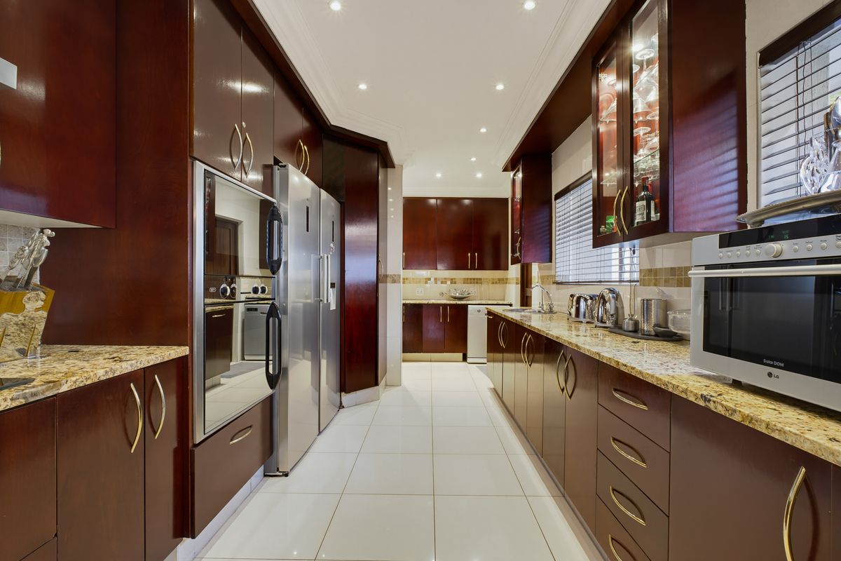 A well-maintained galley-style kitchen featuring dark wood cabinetry, granite countertops, tiled flooring, and integrated appliances with recessed lighting.
