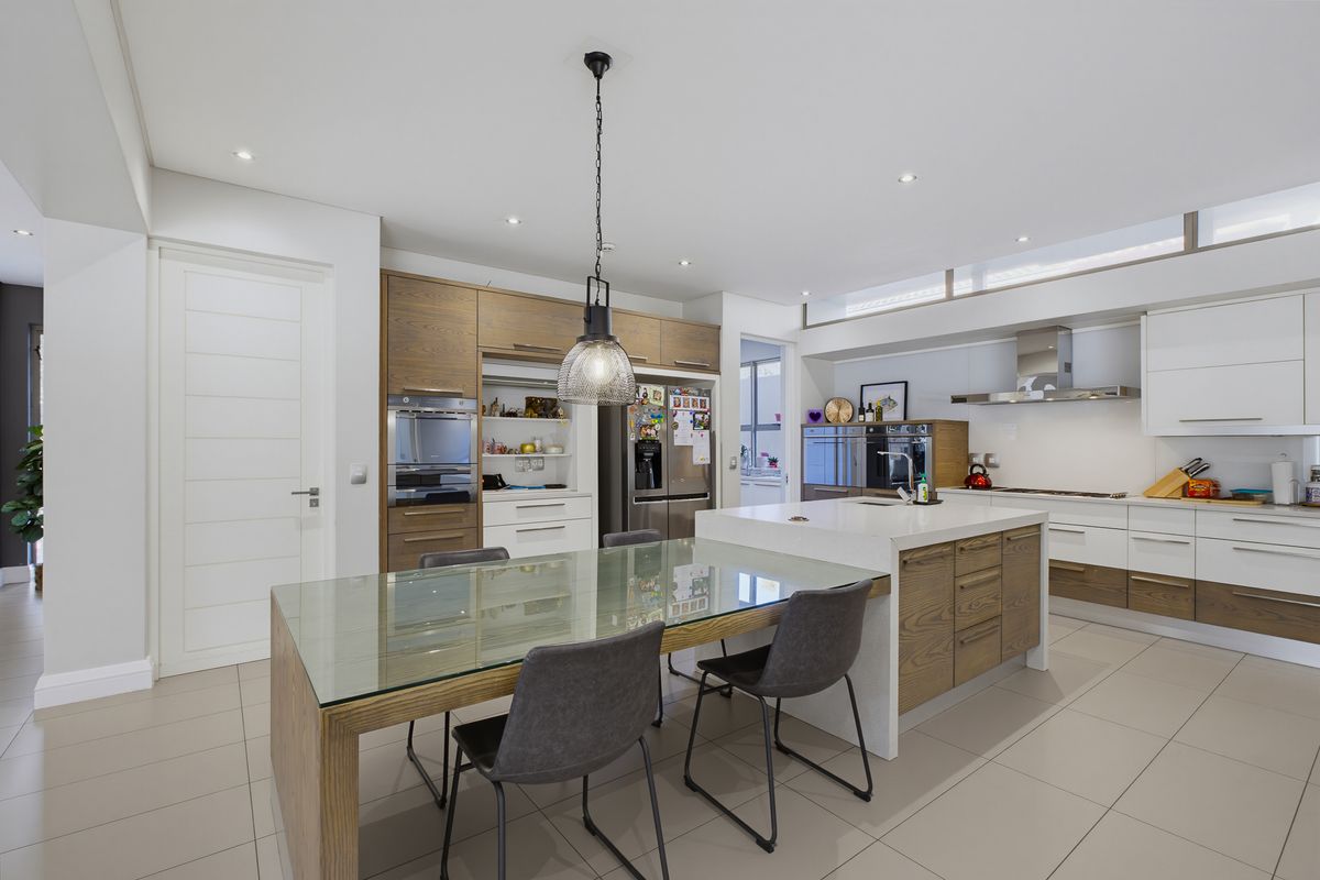 Modern kitchen featuring a central island with integrated dining, high-end built-in appliances, sleek cabinetry, and neutral tiled flooring.