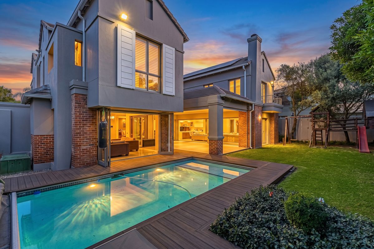 Rear view of a modern cluster home featuring a swimming pool, timber decking, covered patio, and well-maintained garden at dusk.