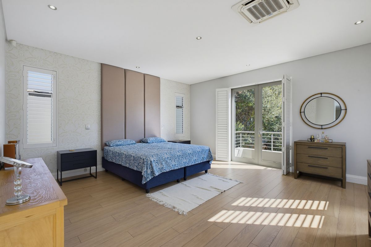 Spacious bedroom featuring light wood-look flooring, recessed lighting, a built-in headboard feature wall, and direct access to a balcony through glass french doors.