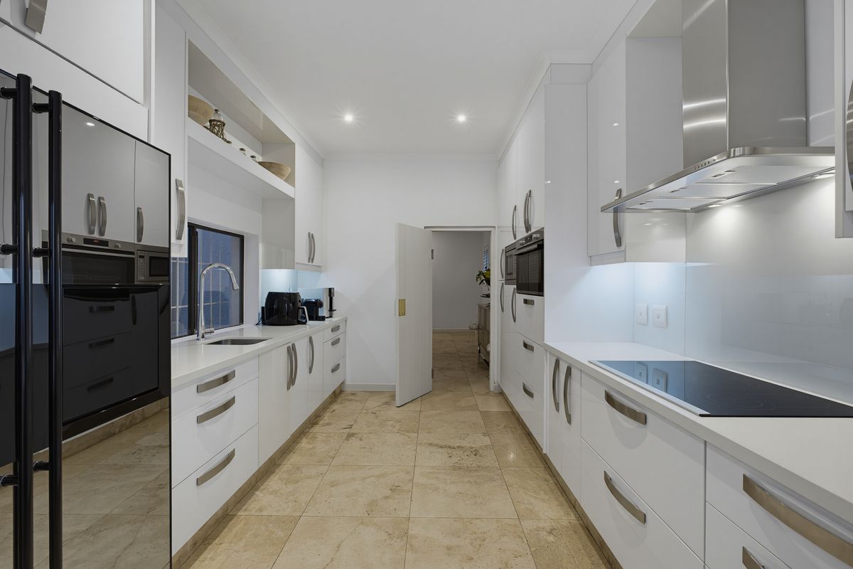 Modern galley-style kitchen featuring sleek white cabinetry, stone countertops, integrated appliances, and high-quality tiled flooring with recessed lighting.
