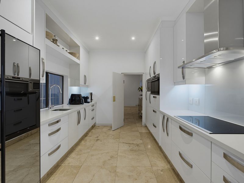 Modern galley-style kitchen featuring sleek white cabinetry, stone countertops, integrated appliances, and high-quality tiled flooring with recessed lighting.