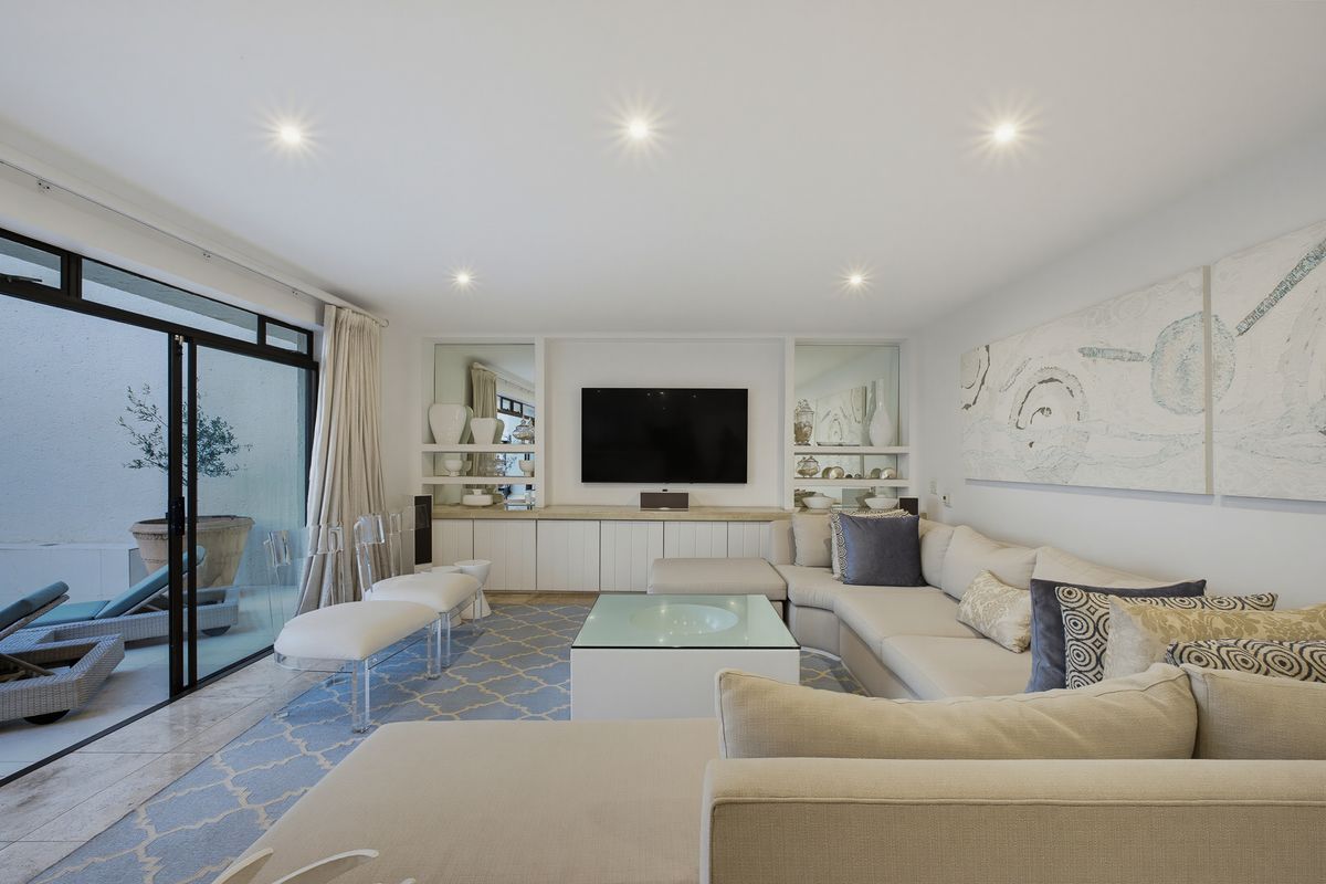 A bright and modern living room featuring built-in cabinetry, recessed lighting, and large sliding glass doors that open onto a private patio area.