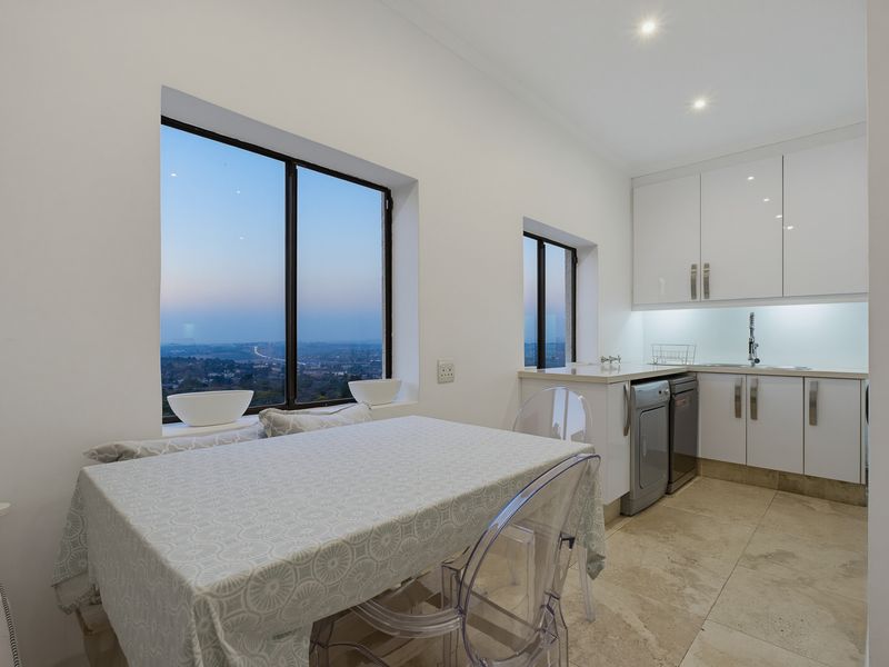 Modern kitchen featuring sleek white cabinetry, stone countertops, and large windows offering expansive views, complemented by neutral tiled flooring and recessed lighting.