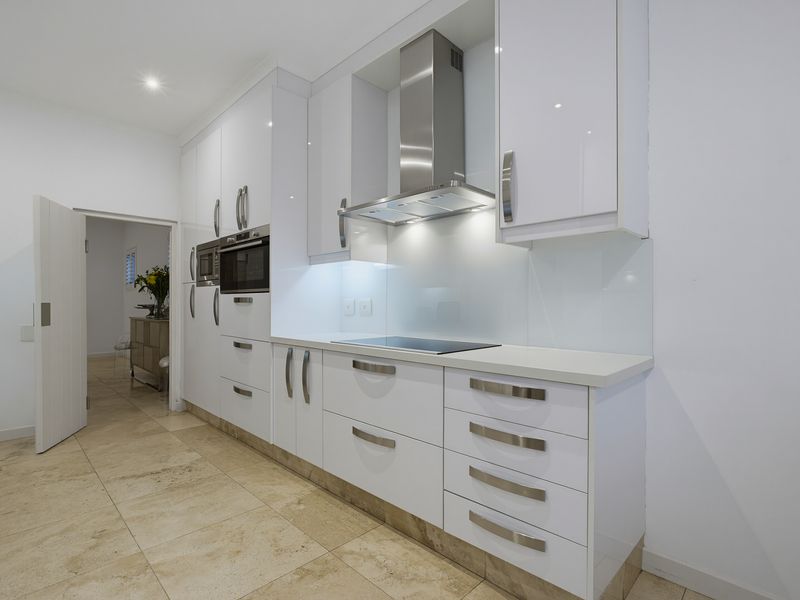 Modern kitchen featuring high-gloss white cabinetry, stone countertops, integrated appliances, and sleek stone flooring with recessed lighting.