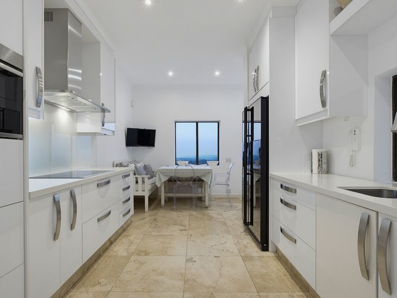 Modern galley-style kitchen featuring sleek white cabinetry, stone countertops, integrated appliances, and high-quality tiled flooring with a bright, contemporary finish.