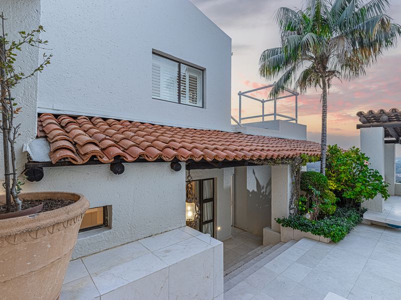 A well-maintained outdoor patio area featuring terracotta roof tiles, stone flooring, and a built-in planter, set against a scenic sunset backdrop.