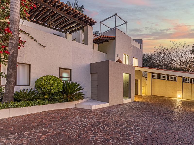 Front elevation of a cluster home featuring a cobblestone driveway, covered carport, and a charming pergola-covered terrace area.