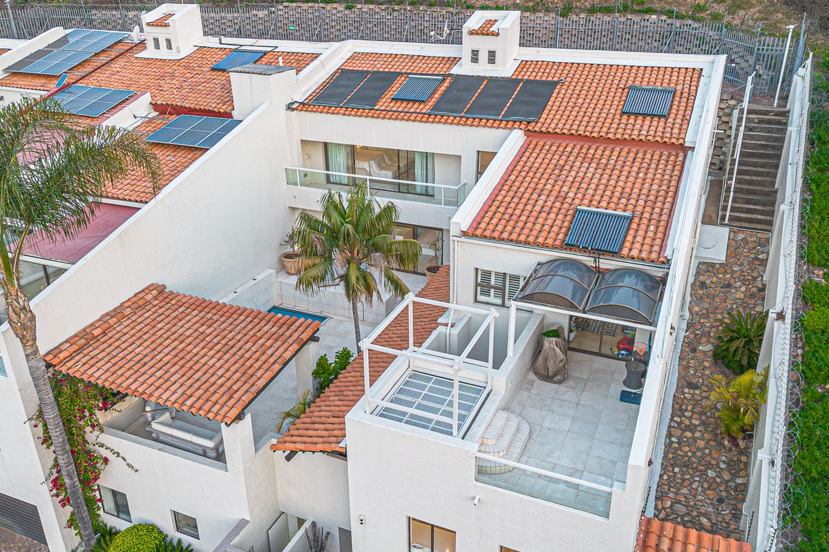 Aerial view of a cluster property featuring terracotta tiled roofs, integrated solar panels, private balconies, a patio area, and a small swimming pool.