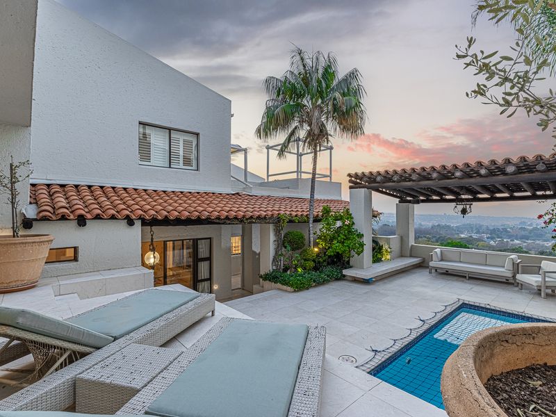 An elegant outdoor pool area featuring a pergola, stone patio, and scenic views, perfect for relaxation and entertaining.
