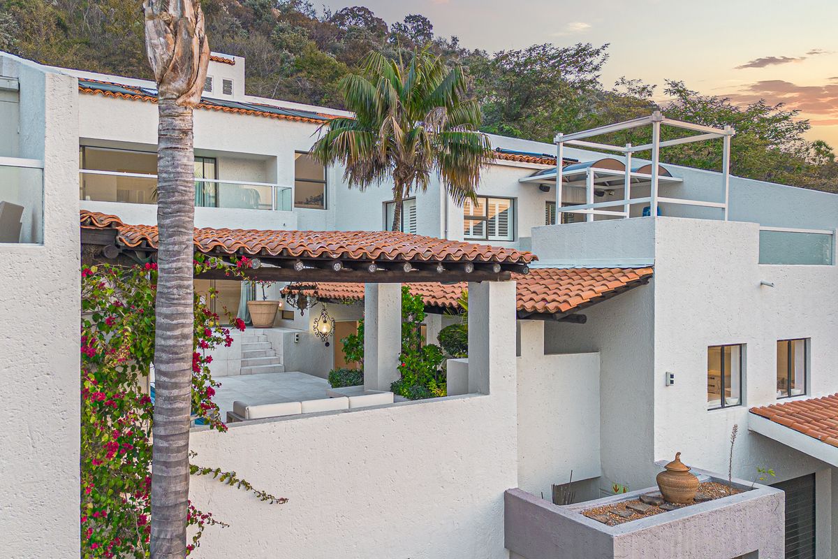 A multi-level rear exterior view of a cluster home featuring terracotta roof tiles, covered patio areas, and modern glass balustrades.