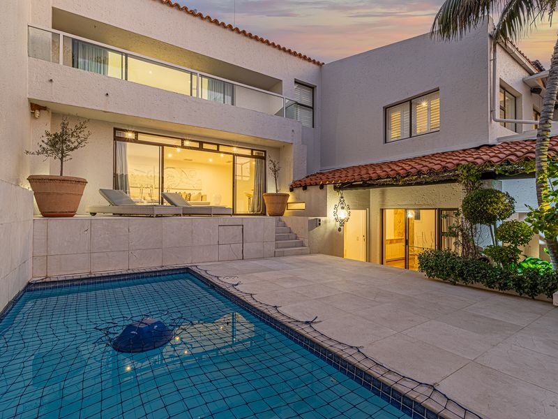 A well-maintained outdoor pool area featuring stone paving, a swimming pool with a safety net, and a multi-level architectural design with terracotta roofing.