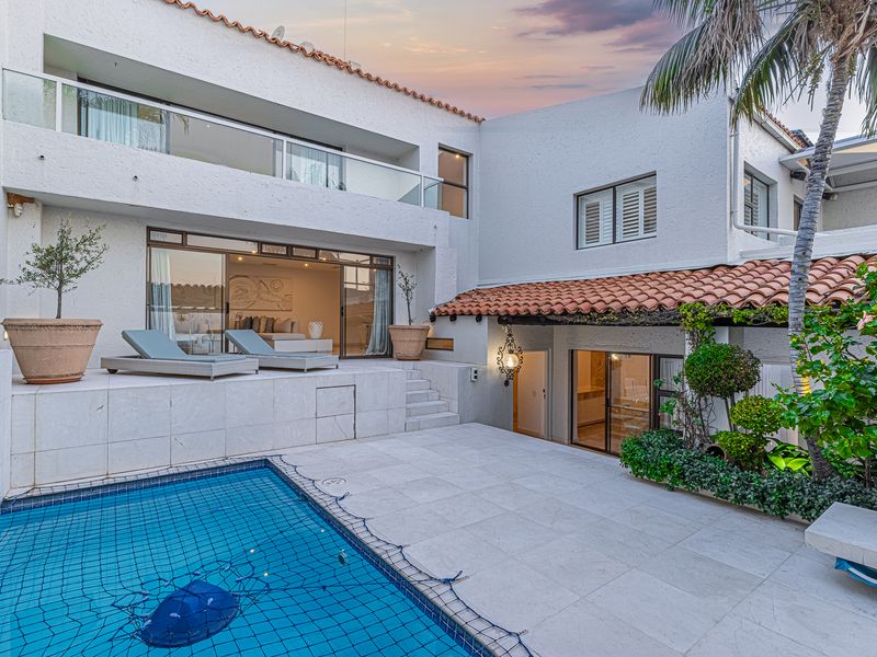 A well-maintained outdoor pool area featuring a tiled patio, glass balustrade balcony, and direct access to the interior living spaces via sliding glass doors.