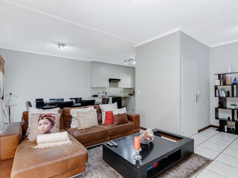 Open-plan living and kitchen area featuring neutral wall finishes, ceramic floor tiles, and functional built-in kitchen cabinetry with an integrated extractor fan.