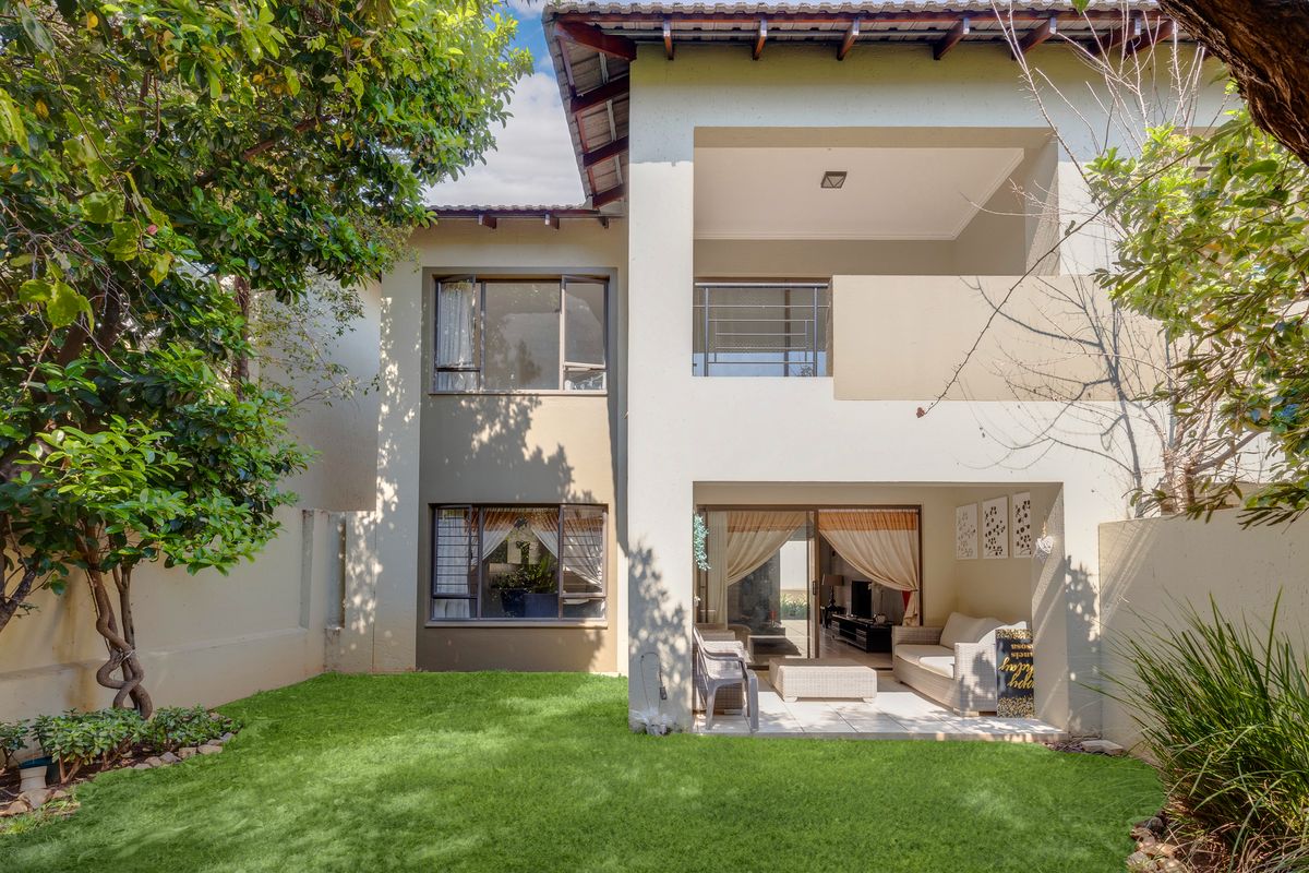 Rear view of the townhouse featuring a covered patio, upper balcony, and a well-maintained private garden area.