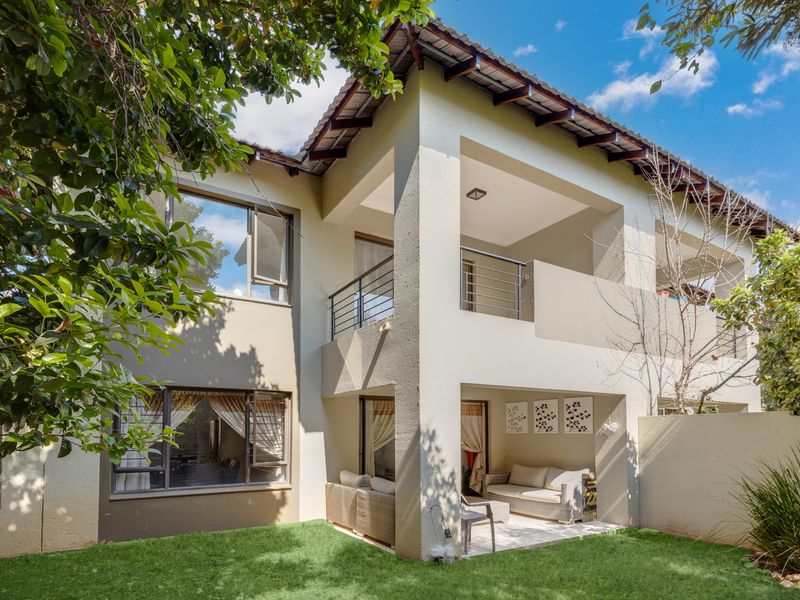 Rear view of a double-storey townhouse featuring a covered ground-floor patio, an upper-level balcony with metal railings, and a private garden area.
