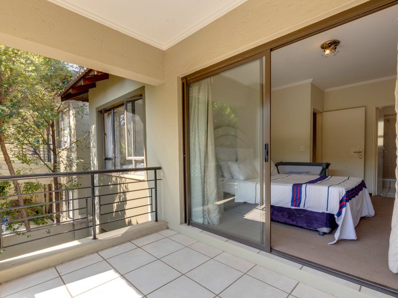 A covered balcony with tiled flooring and a metal balustrade, providing direct access to an interior bedroom through a large sliding glass door.