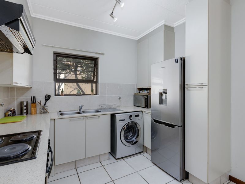 A functional kitchen featuring built-in cabinetry, a double basin sink, electric hob with extractor fan, and tiled flooring with integrated laundry space.