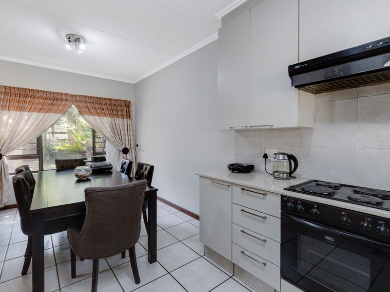 Open-plan kitchen and dining area featuring modern cabinetry, stone countertops, integrated appliances, and tiled flooring with natural light.