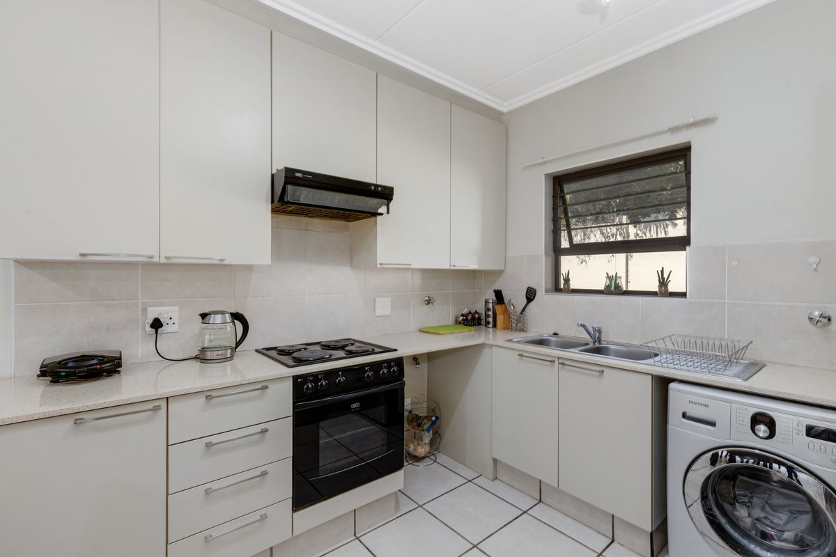 A functional kitchen featuring neutral cabinetry, stone countertops, integrated oven and hob, tiled backsplash, and dedicated space for laundry appliances.