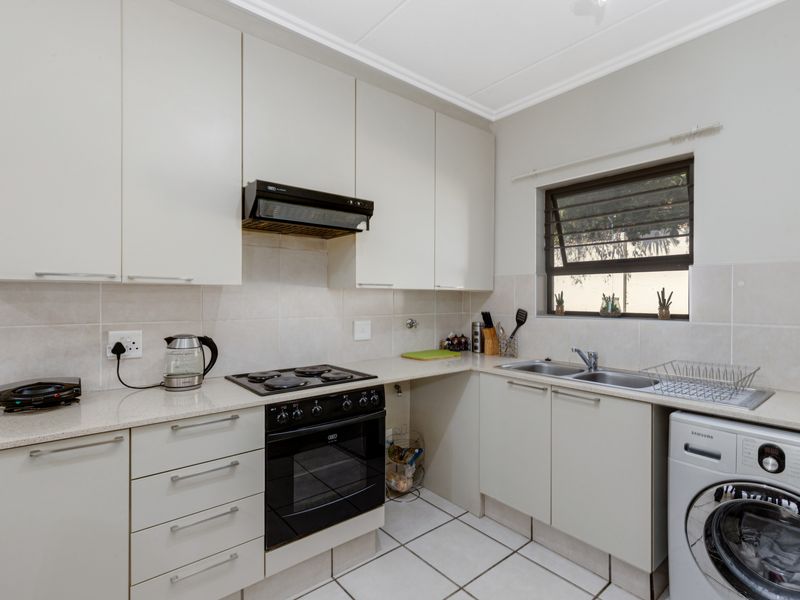 A functional kitchen featuring neutral cabinetry, stone countertops, integrated oven and hob, tiled backsplash, and dedicated space for laundry appliances.