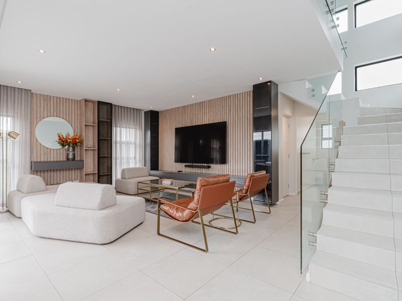 Modern living room featuring slatted timber wall paneling, built-in cabinetry, and a contemporary staircase with a glass balustrade and tiled flooring.