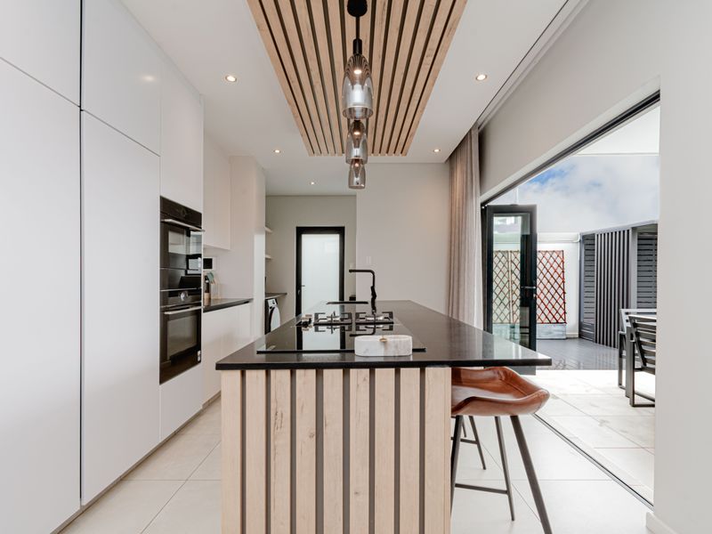 Modern kitchen featuring a central island with a gas hob, built-in appliances, and a stylish slatted timber ceiling detail, opening onto an outdoor patio area.