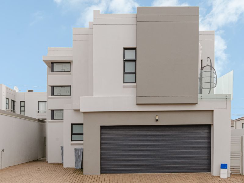 Modern double-story cluster home featuring a sleek facade, paved driveway, automated garage, and an upper-level balcony with glass balustrades.