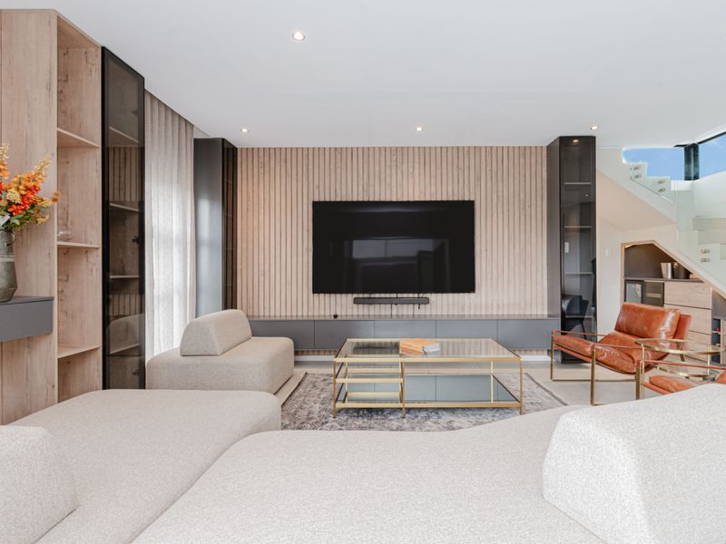 Modern living room featuring sophisticated slatted timber wall paneling, integrated cabinetry, a floating media console, and a contemporary glass staircase.