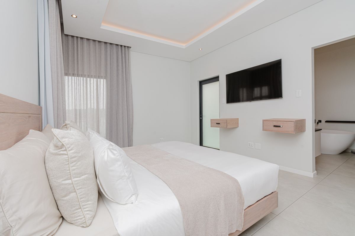 Modern bedroom featuring recessed ceiling lighting, floating bedside tables, tiled flooring, and direct access to an en-suite bathroom.