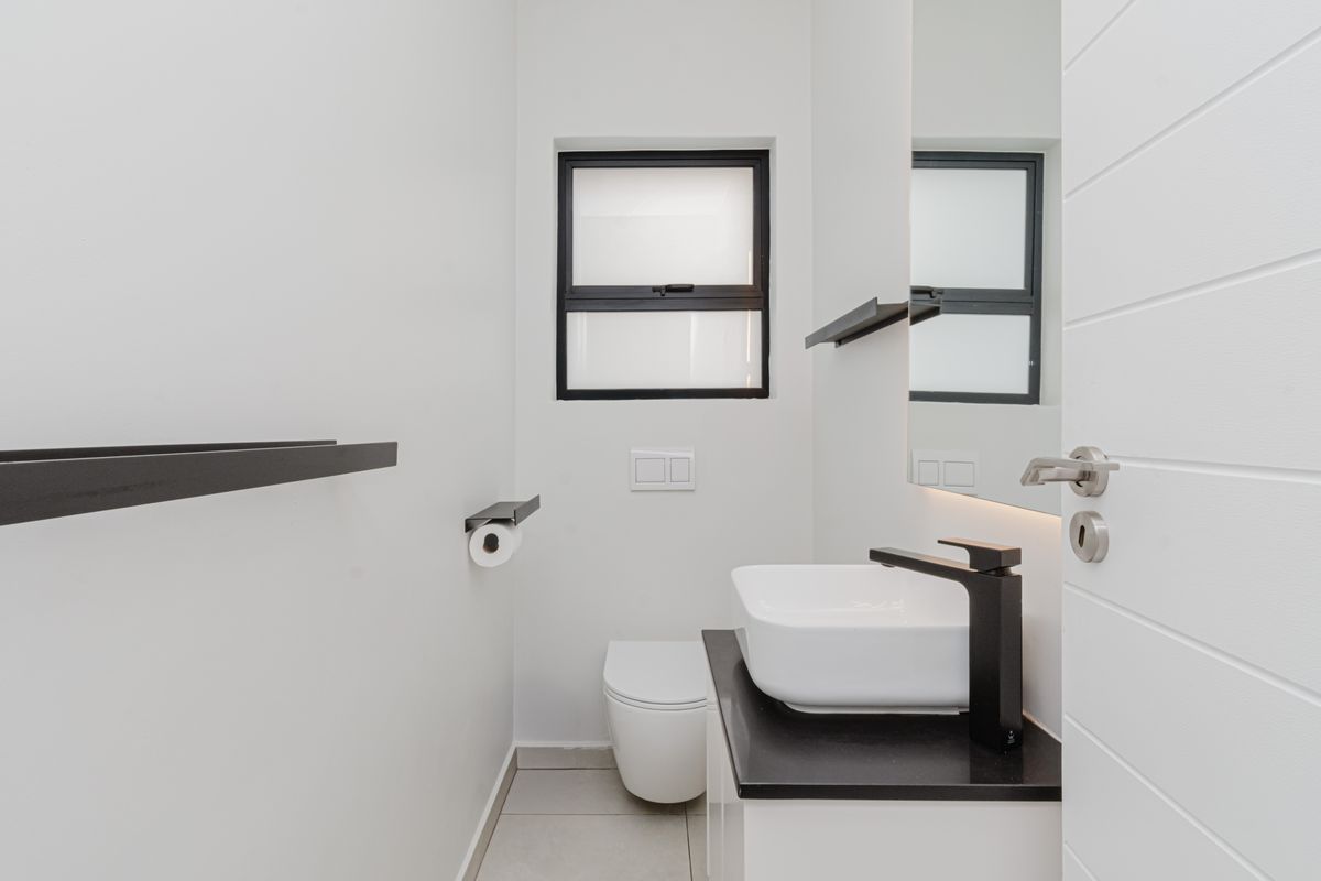 Modern guest bathroom featuring a wall-hung toilet, vessel sink with black fixtures, and a sleek vanity cabinet with a stone countertop.