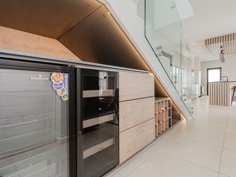Modern open-plan living area featuring a custom under-stair wine storage unit, glass staircase balustrade, and sleek contemporary cabinetry with integrated lighting.