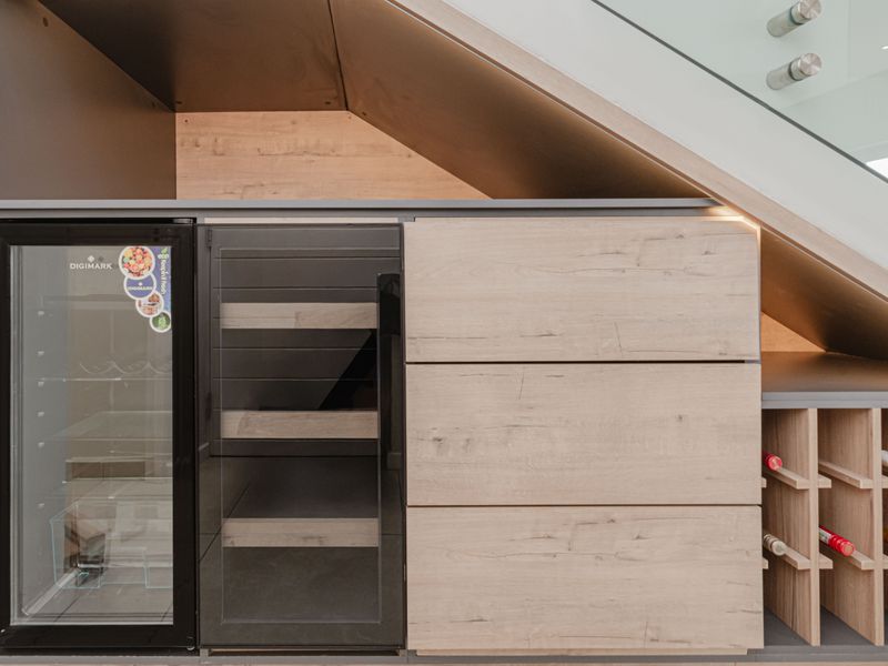 A modern, custom-built wine storage unit integrated into the space beneath the staircase, featuring a built-in wine cooler and dedicated wooden wine racking.
