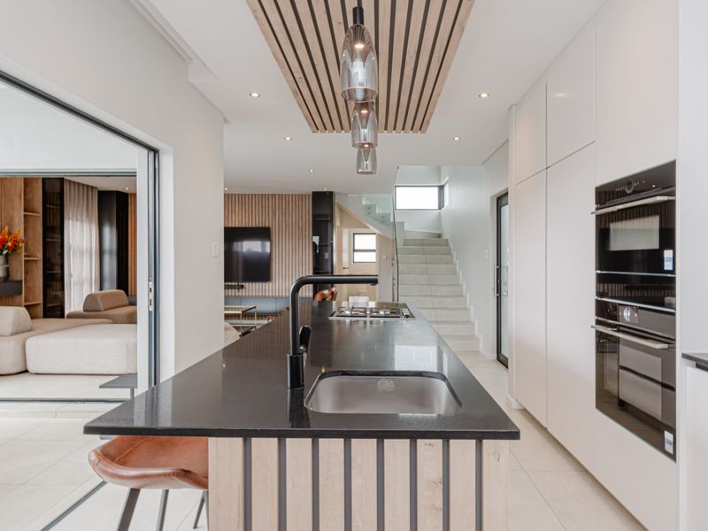 Modern open-plan kitchen featuring a sleek island with stone countertop, integrated appliances, and a striking slatted timber ceiling detail, flowing into the living area.