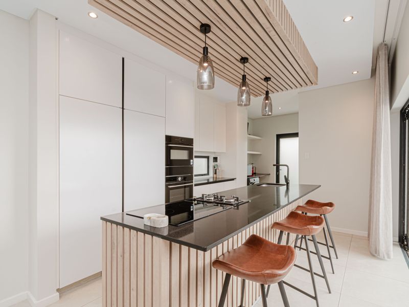 Modern kitchen featuring a central island with stone countertop, integrated appliances, timber slat ceiling detail, and direct access to an outdoor patio area.