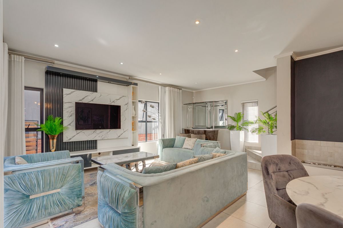 Spacious living room featuring a modern built-in media wall with marble-look detailing, recessed downlights, and tiled flooring.